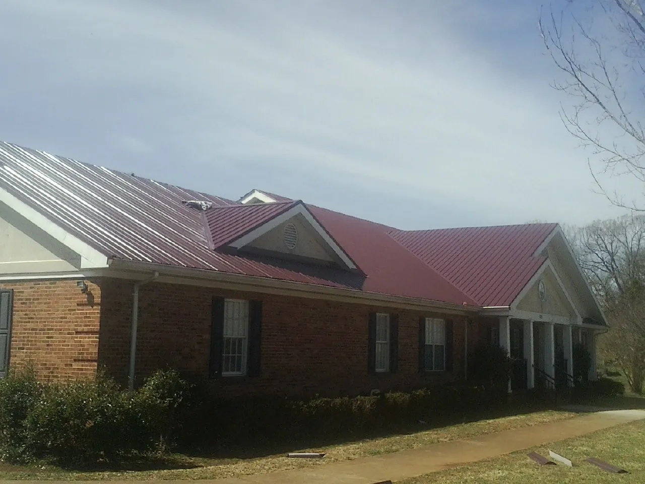 Red metal roof with gabled entries on a long brick building, from a Hail Damage Roof Repair job in Deary