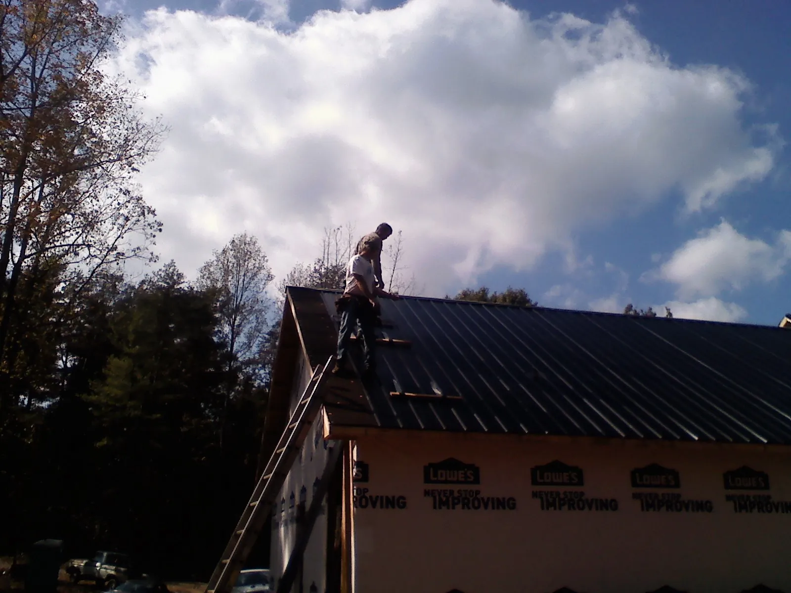 Roofer fastening dark metal panels high against a cloudy sky, from a Roof Inspection job in Deary