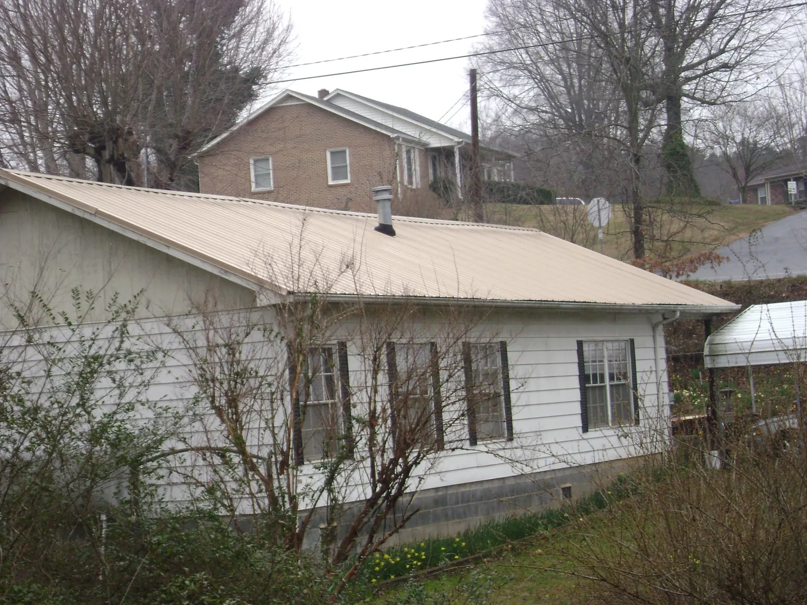 Tan metal roof on a white sided house set into a hillside — Commercial Roofing by Roofing Brothers in Deary